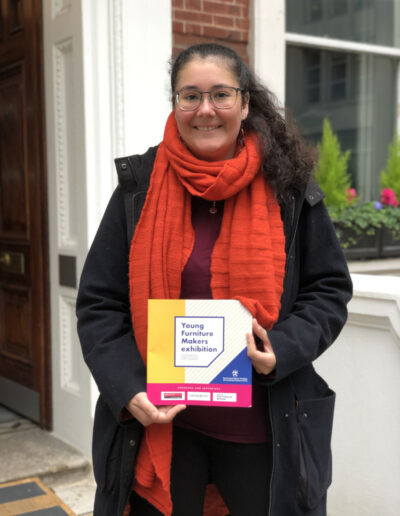 Chaska Schuler vor dem Gebäude der Furniture Makers' Company in London mit dem Ausstellungsprogramm der Young Furniture Makers Exhibition 2022.