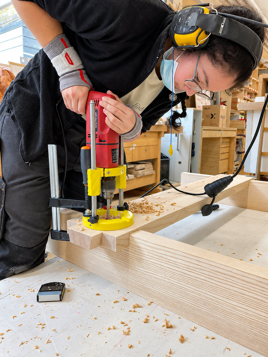 Japanische Holzverbindung Watari ago – Schreinerlehre 2021 Chaska Schuler bohrt während ihrer Schreinerlehre mit einem Bohrständer die Löcher für verkeilte Runddübel an der japanischen Holzverbindung Watari ago eines Massivholzbetts.