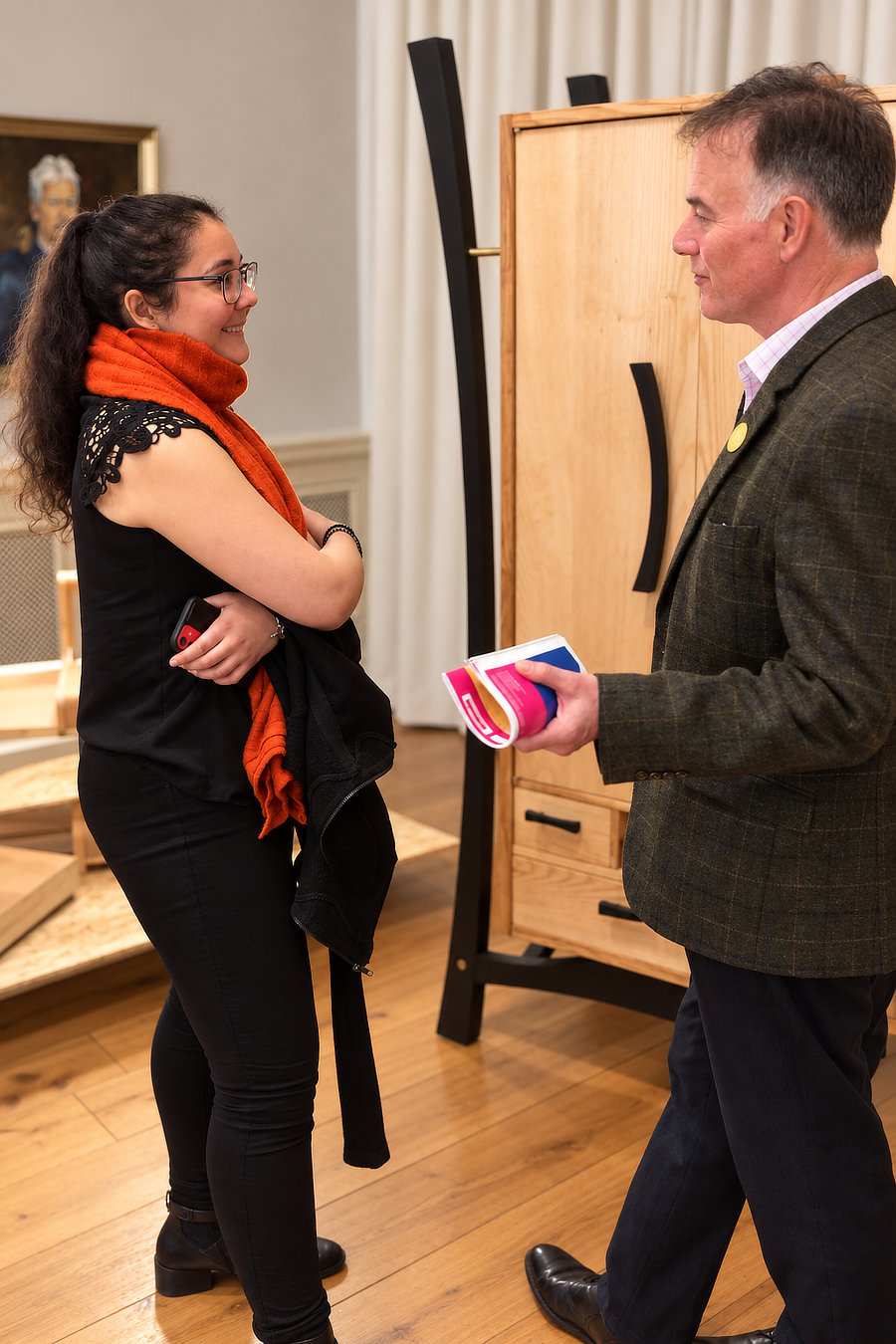 Young Furniture Maker Award 2022 – Chaska Schuler in London Chaska Schuler im Gespräch mit einem Ausstellungsbesucher vor ihrem Kleiderschrank «Licht und Dunkel» beim Young Furniture Maker Award 2022 in London.